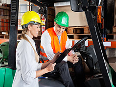 Female supervisor showing clipboard to colleague sitting in forklift at warehouse